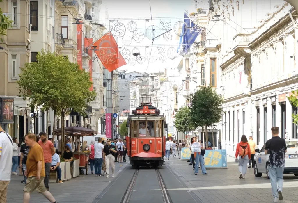 Historic red tram on İstiklal Street in Istanbul, with pedestrians and historic buildings.