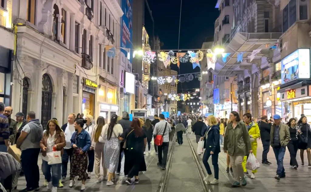A view of the evening crowds on Istiklal Street, with people walking and shopping under city lights.