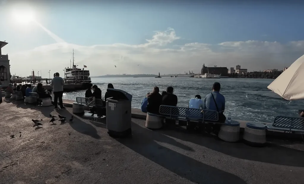 Kadıköy shore in September near the ferry station, with ferries and people strolling by.