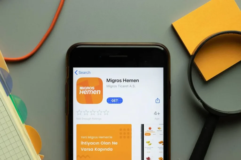 Close-up of the Migros Hemen mobile app logo on a phone screen, representing the convenience of online grocery shopping in Turkey.