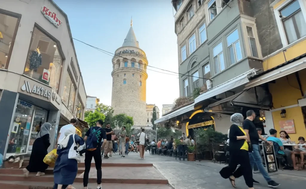 View of Galata Tower from a narrow street, surrounded by cafés, shops, and historic buildings.