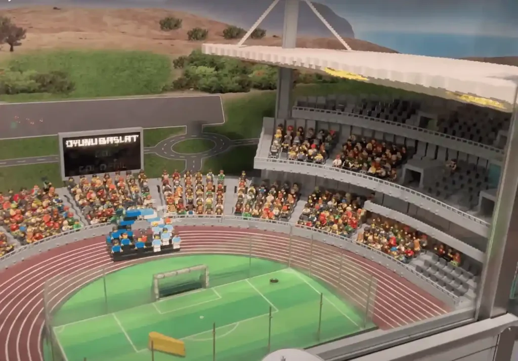 A detailed LEGO stadium miniature at Legoland, featuring stands, a playing field, and tiny LEGO spectators and players. The model mimics a real-life sports arena, with surrounding miniature buildings and landscaping.